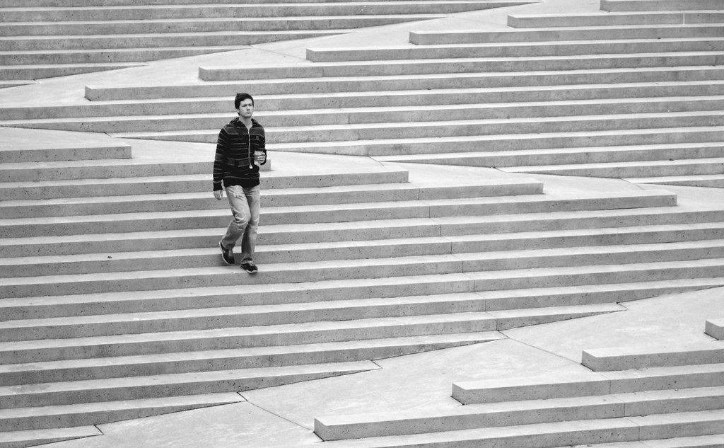 Image of a stramp. A 1-story stair made of concrete blocks, with a 60 m long ramp zigzagging and interrupting the stairs. A man is walking down the stairs.
